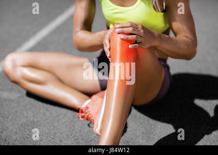 Sezione bassa di sportive che soffrono di dolori articolari seduti sulla via durante la giornata di sole Foto Stock