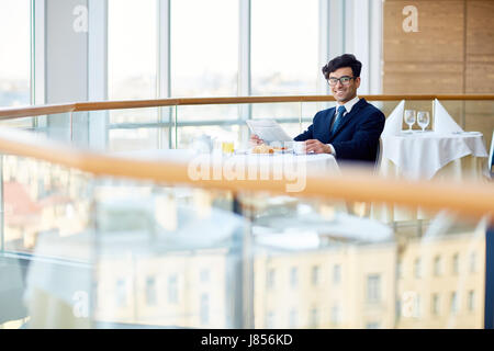 Successo imprenditore giovane con quotidiano avente la prima colazione nella caffetteria Foto Stock