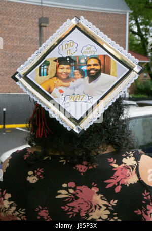 Una giovane donna sulla strada per la sua festa di laurea indossando un cappello riconoscendo l'aiuto del suo un altro significativo e bambino. In Bayside, Queens, NYC Foto Stock