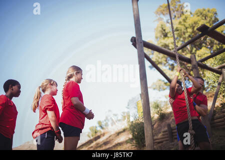 Il Trainer assiste un capretto a salire su una corda in boot camp in una giornata di sole Foto Stock