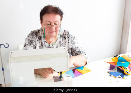 Patchwork e la trapuntatura presso la bottega di un sarto donna su sfondo bianco - donna con gli occhiali cuce sulla macchina per cucire dei frammenti di tessuti colorati per patchworking. Foto Stock