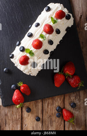 Dolci Rotolo alle fragole con panna montata, menta e mirtilli vicino sul tavolo. Vista verticale da sopra Foto Stock