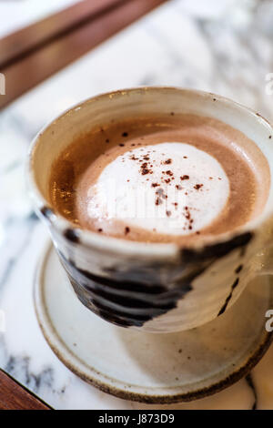 Hot caffè moca e rabboccato con polvere di cacao in argilla tazza ceramica collocati sul piano di marmo tabella Foto Stock