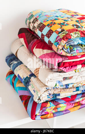 Patchwork, trapuntatura e fashion concept - close-up sul bellissimo colorate coperte ripiegate e memorizzati in diverse righe in altezza per lo stoccaggio e la vendita di cucito prodotti tessili su sfondo bianco. Foto Stock