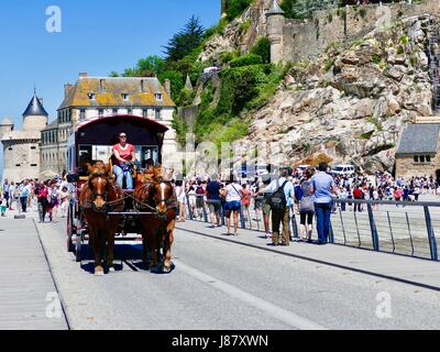 Il team di cavalli tira il carrello pieno di visitatori lasciando Mont Saint-Michel, passando ai pellegrini che sono appena arrivati. Folle a Mont Saint Michel, Francia Foto Stock