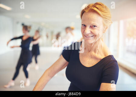 Donna matura sorridente e guardando la telecamera durante l'esecuzione di balletto in classe. Foto Stock