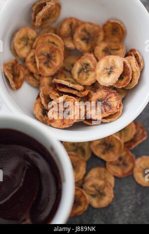 Banana chips in una tazza di cioccolato dip Foto Stock
