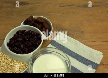 Tre-chambered piatto bianco con i fiocchi d'avena, essiccato di mirtillo palustre e albicocche secche e una ciotola di vetro con latte fresco. Sana colazione set. Chiudere, orizzontale Foto Stock