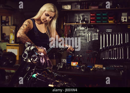 Donna bionda meccanico che lavora in un laboratorio del motociclo Foto Stock
