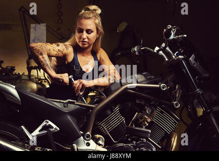 Donna bionda meccanico riparazione di un motociclo in un workshop Foto Stock