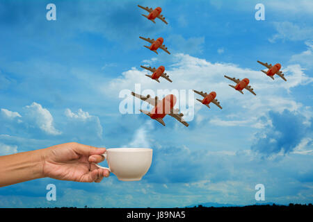 Mano azienda tazza da caffè con modelli di aereo su sfondo cielo, pianificazione del viaggio concetto. Foto Stock