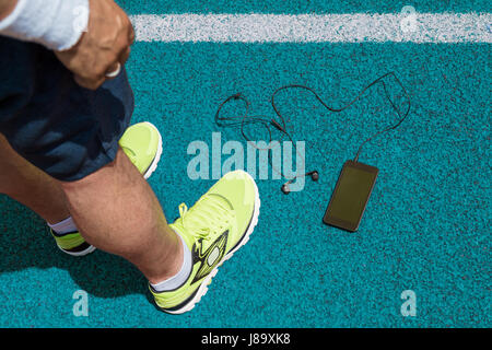 Gambe maschio con esecuzione di sneakers, smartphone con schermo vuoto e cuffie intrauricolari su blu acceso via. Parte superiore verso il basso punto di vista. Sport, tecnologia, Foto Stock