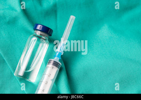 Siringa medica e fiale giacente sull'ospedale sfondo verde. Lo sfondo può essere una parte di tessili di un medico o un infermiere uniforme di lavoro Foto Stock