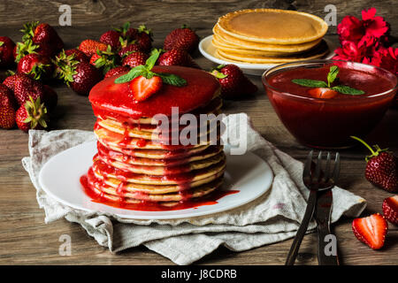 American pancake e salsa di fragole su uno sfondo di legno. Grande profondità di campo. Foto Stock