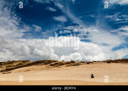 Donna meditando sulla spiaggia di Guincho sotto incredibile cielo, Cascais, Portogallo Foto Stock