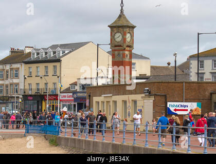 Morecambe Bay Clock Tower, Lancashire, Regno Unito. Il sole può romparsi mentre i vacanzieri, i turisti e i visitatori si godono le attrazioni sul lungomare. Foto Stock