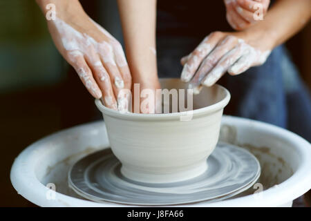 Madre figlio insegna a lavorare sulla ruota di ceramiche. Close up di mani sporche scultura in argilla. Foto Stock