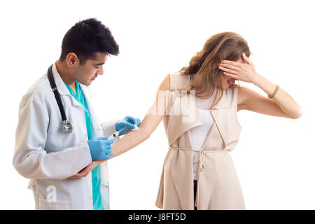 Bel giovane medico con i capelli neri in abito bianco con uno stetoscopio e guanti blu facendo una iniezione di giovani spaventata donna con capelli lunghi marrone in Foto Stock