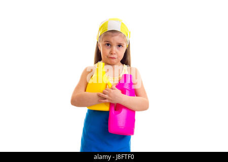 Triste bambina con lunghi capelli castani in maglietta gialla e grembiule blu con fazzoletto giallo tenendo giallo e rosa bottiglie su sfondo bianco in stu Foto Stock