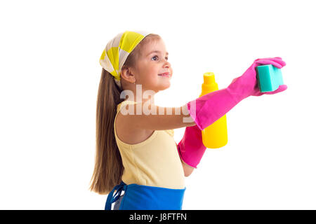 Poco carino ragazza con lunghi capelli castani in maglietta gialla e grembiule blu con rosa guanti e fazzoletto giallo azienda spugna verde e giallo sulla bottiglia Foto Stock