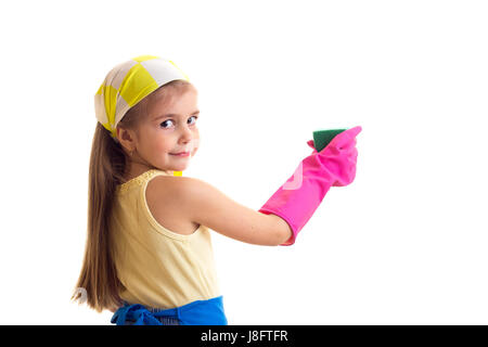 Poco piacevole ragazza con lunghi capelli castani in maglietta gialla e grembiule blu con rosa guanti e fazzoletto giallo azienda spugna verde e giallo bottl Foto Stock