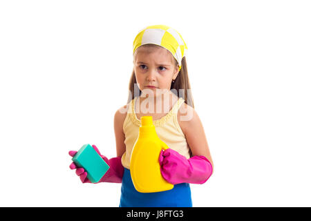 Piccola ragazza triste con lunghi capelli castani in maglietta gialla e grembiule blu con rosa guanti e fazzoletto giallo tenendo in spugna e bottiglia di colore giallo su bianco Foto Stock