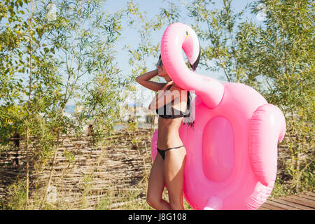 Allegro giovane e bella donna millenario holding spruzzata rosa fenicottero gonfiabile galleggiante in estate. 20s Foto Stock