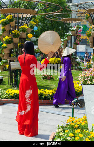 La città di Ho Chi Minh, Vietnam - Febbraio 07, 2016: due giovani donne vietnamita in tradizionale Ao Dai sono vestito che posano per una foto davanti aiuole di fiori a Foto Stock