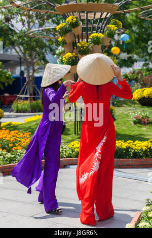 La città di Ho Chi Minh, Vietnam - Febbraio 07, 2016: due giovani donne vietnamita in tradizionale Ao Dai sono vestito che posano per una foto davanti aiuole di fiori a Foto Stock