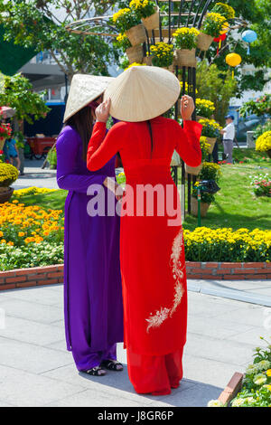 La città di Ho Chi Minh, Vietnam - Febbraio 07, 2016: due giovani donne vietnamita in tradizionale Ao Dai sono vestito che posano per una foto davanti aiuole di fiori a Foto Stock