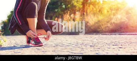 Runner donna sua legatura lacci delle scarpe durante il jogging - Sport e Fitness al tramonto Foto Stock