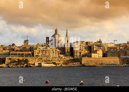 Tramonto sulla Floriana, Valletta, Malta. St Pauls Co-cattedrale guglia e la cupola della Basilica di Nostra Signora del Monte Carmelo. Visto da di Sliema. Foto Stock