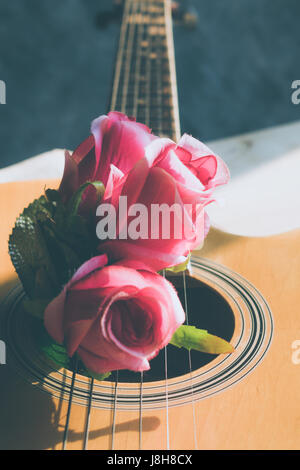 Rose fiori su un libro con una chitarra su una tavola di legno. Foto Stock