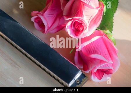 L'armonica con un fiore rosa su un sfondo di legno. Foto Stock