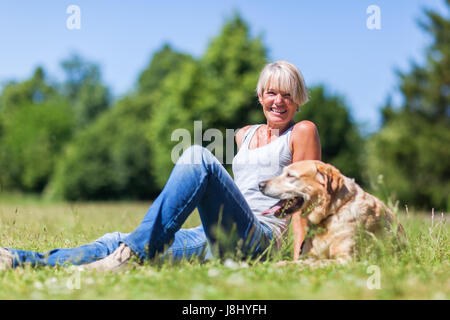 Sorridente coppia donna seduta con un Labrador Retriever cane sul prato Foto Stock
