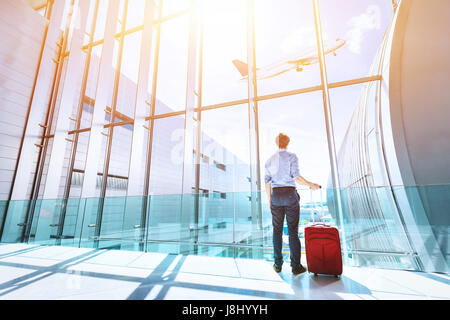 Imprenditore all'aeroporto terminale gate di imbarco guardando aereo attraverso la finestra Foto Stock