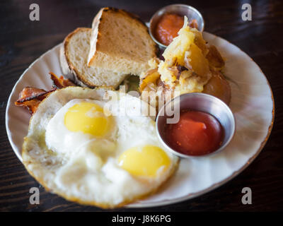 Due lato soleggiato di uova, hash brown patate, pasta madre il pane tostato e pancetta (Canadian prima colazione da Chartier Ristorante a Beaumont, Alberta, Canada. Foto Stock