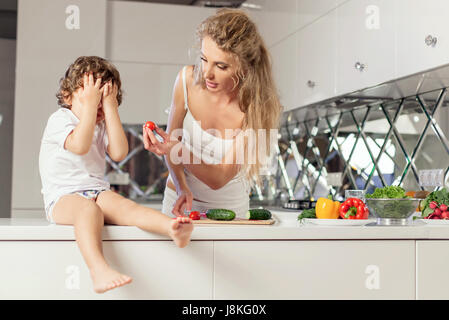 Madre bella mostra qualcosa al suo piccolo figlio. Ragazzo nasconde il viso con le mani. Foto Stock