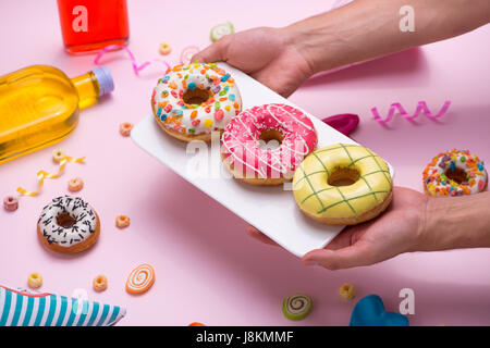 Parte. Lato piastra di contenimento di zuccherini colorati vetrate rotonde ciambelle e bottiglie di bevande su sfondo rosa. Foto Stock