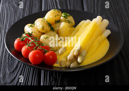 Asparagi bianchi con salsa olandese, le patate di primizia e i pomodori di close-up su una piastra orizzontale. Foto Stock