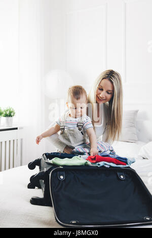 Viaggiare con i bambini. Felice madre con il suo bambino abiti di imballaggio per le proprie vacanze Foto Stock