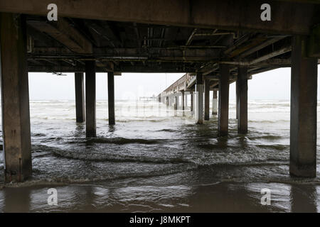 Le onde del mare di laminazione e di rottura sulla spiaggia con sabbia sotto i supporti in legno di un lungo molo che si allunga verso il lontano orizzonte Foto Stock