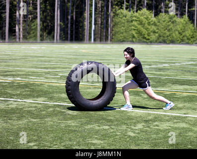 Teen età ragazza di spinta pneumatico di grandi dimensioni sul campo sportivo per costruire la forza Foto Stock