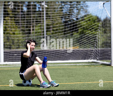 Teen età ragazza in appoggio mentre su un campo di calcio durante la luminosa giornata calda Foto Stock