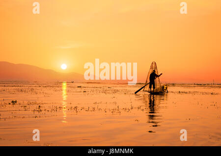 Silhouette di un pescatore birmano sulla barca di bambù al tramonto. Lago Inle, Myanmar (Birmania), meta di viaggio Foto Stock