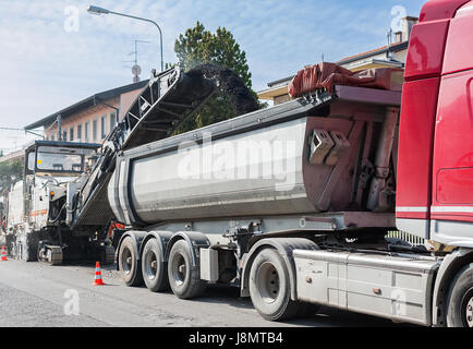 La costruzione di strade, asfaltatura di una strada. Dumper è caricato con asfalto fresato da pialla a freddo la macchina. Foto Stock