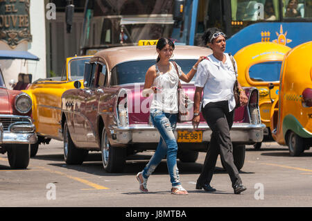 L'Avana - circa giugno, 2011: pedoni a piedi tra il colorato American taxi auto e luminose 'cocotaxi' rickshaw veicoli in Centro. Foto Stock