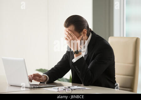 Imprenditore stanco alla scrivania con computer portatile ricerca via per uscire dalla difficile situazione. Riflessivo ha sottolineato frustrato uomo che lavora per troppo tempo sul computer, Foto Stock