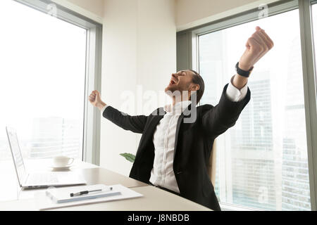 Happy businessman alza le mani, urlando, estasiato guy sente gioia al banco nella parte anteriore del pc portatile. Imprenditore positivo celebrando la vittoria con apertura di un Foto Stock
