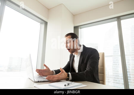 Imprenditore a scrivania guardando lo schermo del notebook con sorpresa. Uomo in ufficio sconvolto con esclusivo a basso prezzo offerta, vendita o sconto enorme in online sh Foto Stock